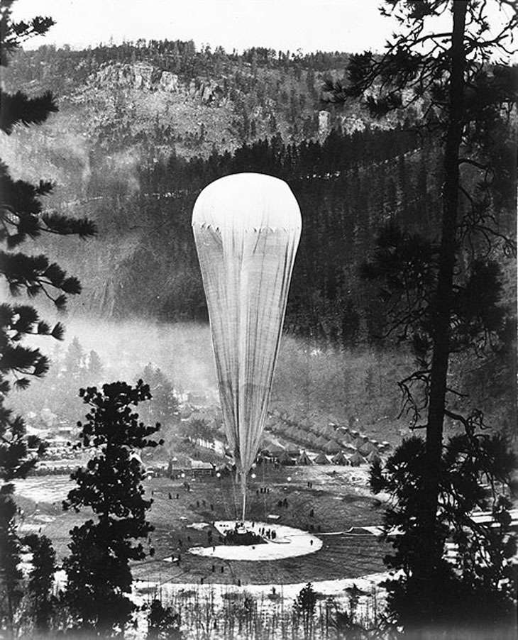 Black and white photo of a helium balloon being inflated in the forest.