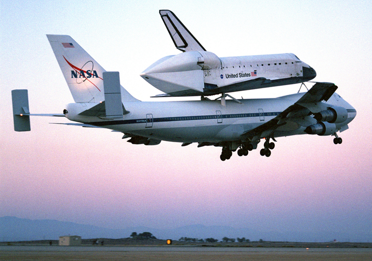 The space shuttle is carried atop a larger plane.  As it flies a covering can be seen over the entire back of the shuttle.
