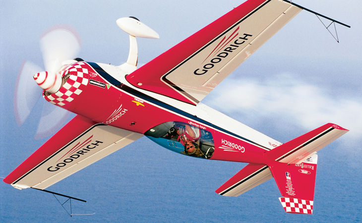 A man flies upside down in a brightly colored checkered plane.