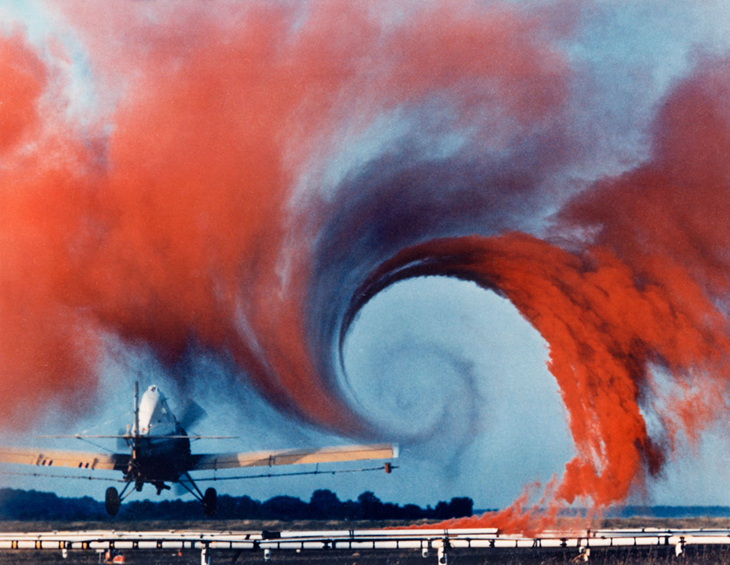 Red smoke spirals around the upper tip of an airplane wing.