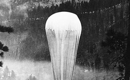 Black and white photo of a helium balloon being inflated in the forest.