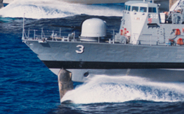 Hydrofoils at the front and back of two military boats lift the hulls of the boats out of the water as they speed forward.
